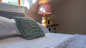 Un lit bien fait, avec une tête de lit à rayures, un coussin vert à texture et une couverture blanche. On y trouve une table de chevet avec une lampe et un vase rempli de fleurs.
