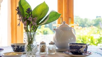 A table set with a vase of flowers, a teapot, cups, and salt and pepper shakers.