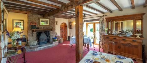 A dining area with a red carpet, wooden beams, a fireplace, and a table set for a meal.
