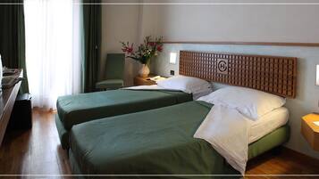 Une chambre d’hôtel avec deux lits, un bureau avec une chaise, une télévision, une lampe et un vase avec des fleurs.