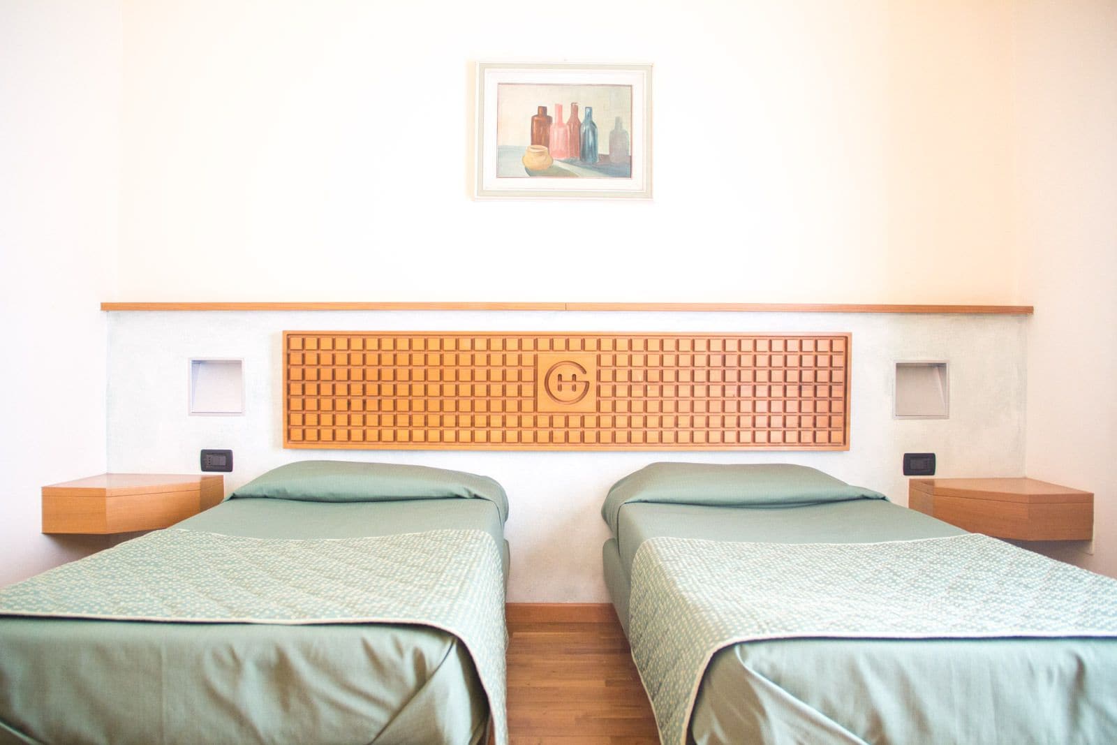 A room with two beds, a wooden headboard with a grid pattern, a framed picture on the wall, and bedside tables with lamps.