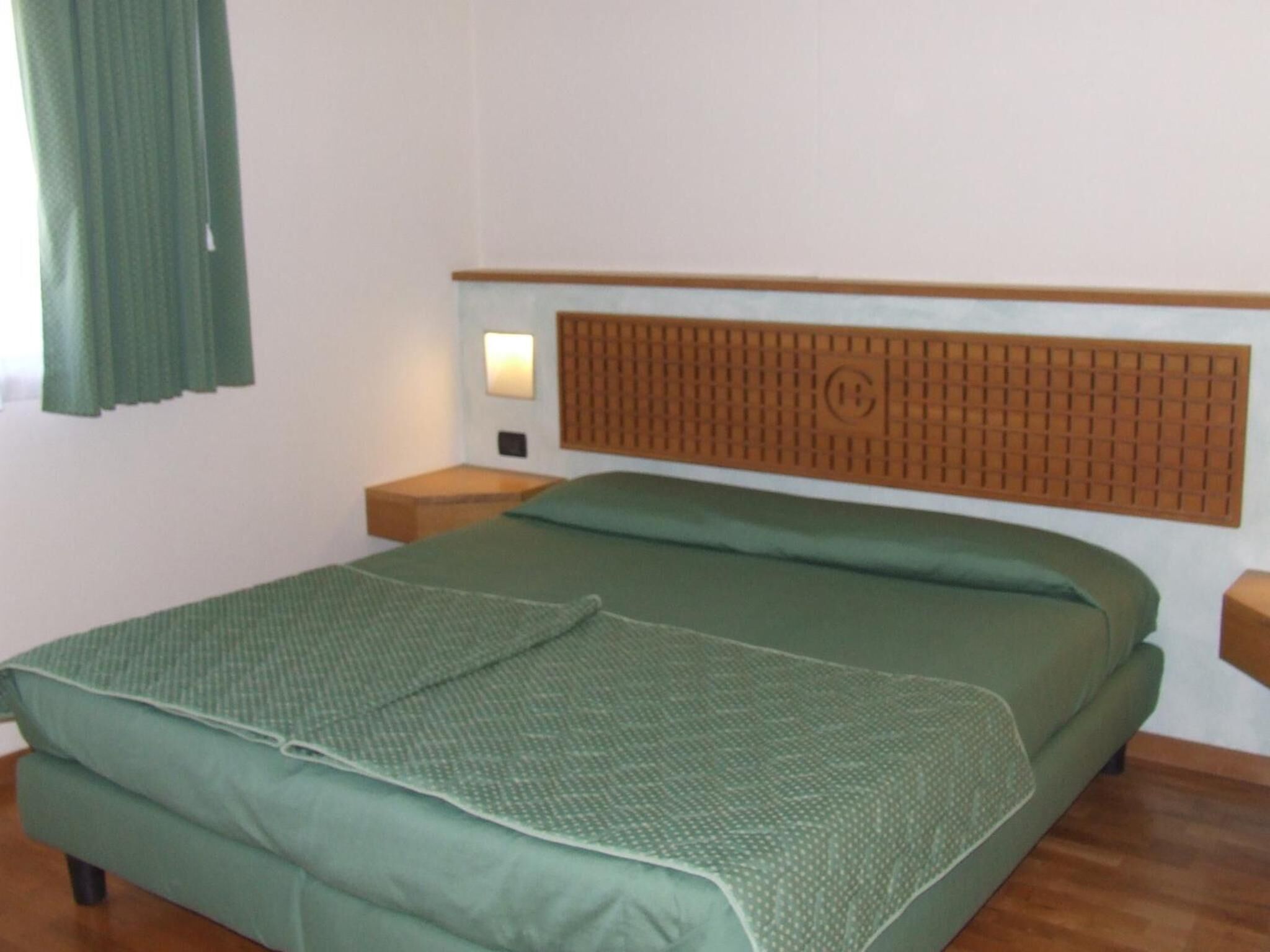 Une chambre avec un lit simple, une tête de lit en bois, une table de chevet et une petite table de nuit.