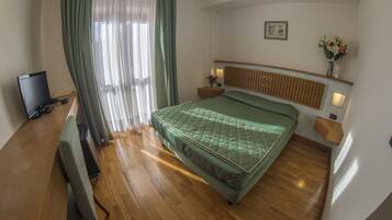A hotel room with a bed, a desk with a computer, a TV, and a window with curtains.