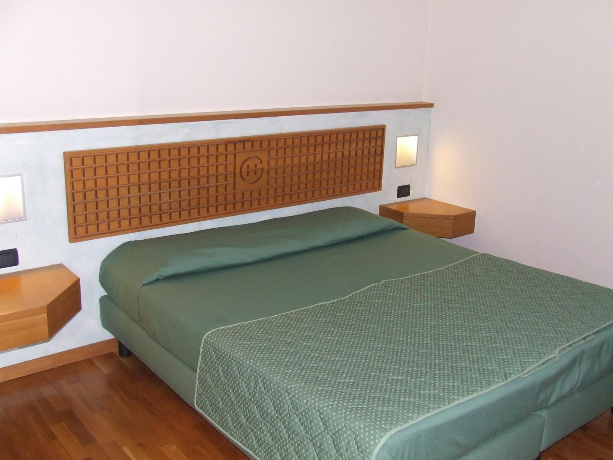 Een eenpersoonskamer met een houten hoofdeinde, twee nachtkastjes en een groene sprei.