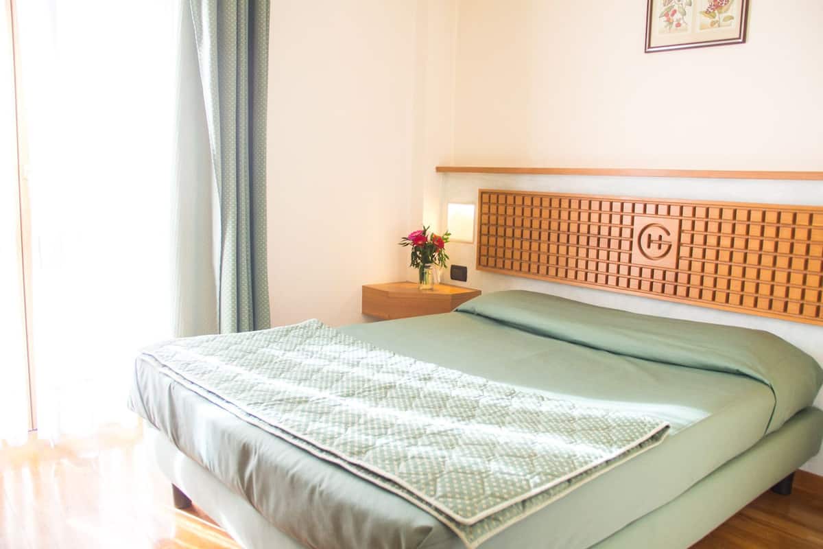 Una cama bien hecha con una colcha estampada, un cabecero de madera y una mesita de noche con un jarrón de flores.
