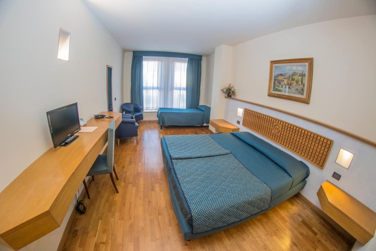 Habitación de hotel con cama, escritorio, silla y un ventanal con cortinas.