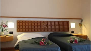 A hotel room with two beds, a wooden headboard with a logo, bedside tables with lamps, and floral decorations.