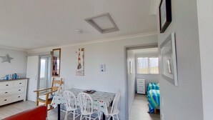 Une pièce comprenant une table à manger, des chaises, une commode, un miroir et un lit recouvert d’une couvre-lit à rayures.