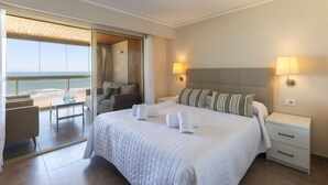 Ett hotellrum med en stor säng, två sänglampor, utsikt över stranden och en balkong med sittplatser.