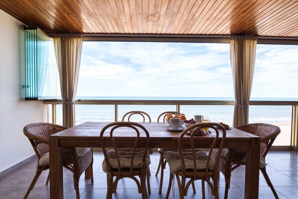 A dining area with a wooden table and wicker chairs, overlooking the sea.