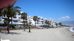 Un hotel frente al mar con varios pisos, palmeras y una playa al fondo.