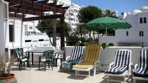 Un patio exterior con sillones blancos, una mesa y una sombrilla verde.