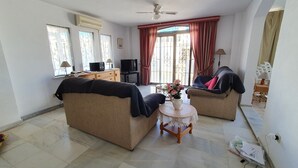 Una sala de estar con dos sofás, una mesita redonda con un florero, un ventilador de techo y un televisor sobre un mueble bajo.