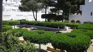 Un patio con setos bien cuidados, algunos árboles y edificios blancos al fondo.