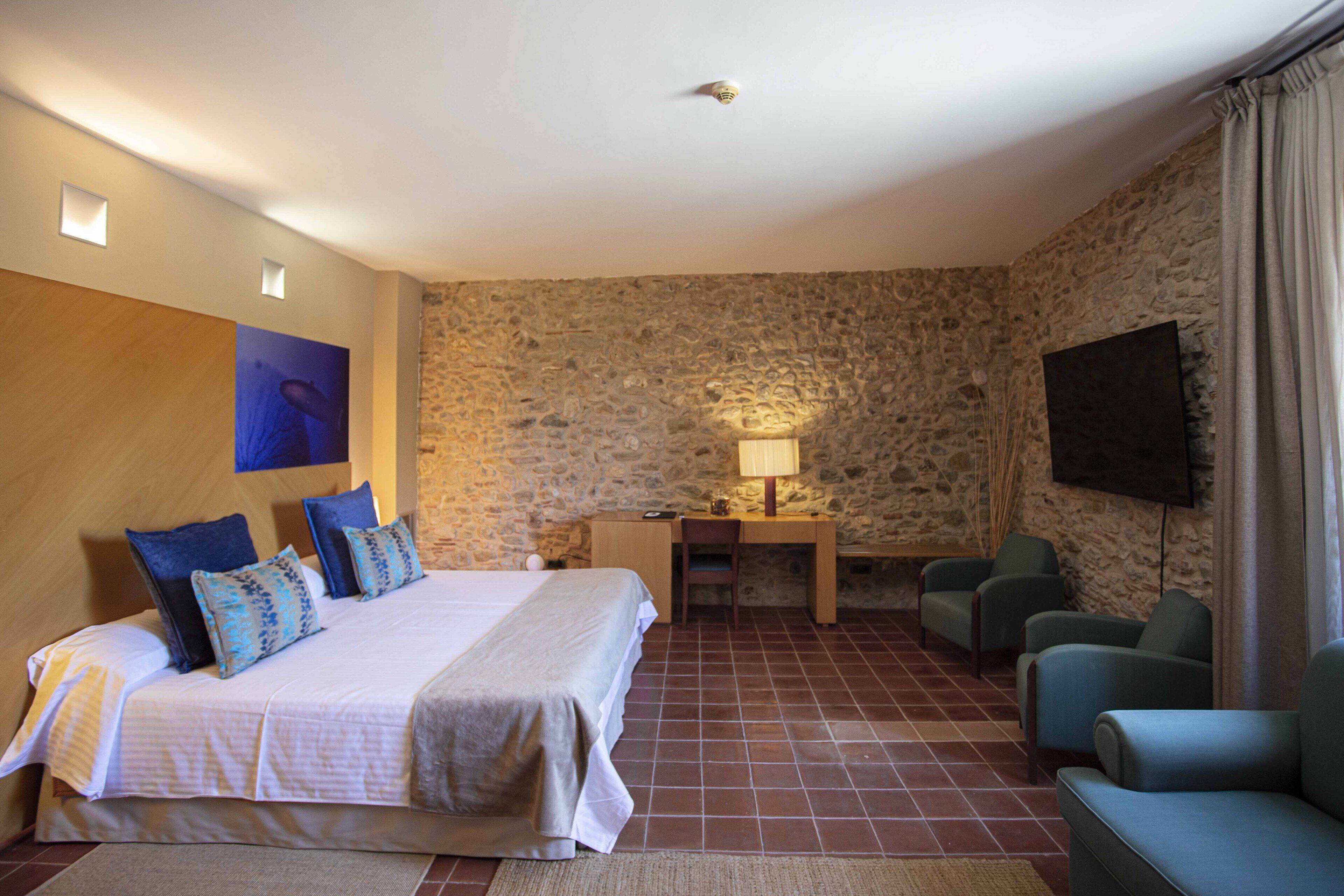 Een hotelkamer met een bed, een bureau, een stoel, een televisie en stenen muren.