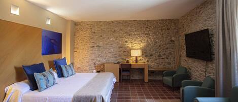 Een hotelkamer met een bed, een bureau, een stoel, een televisie en stenen muren.