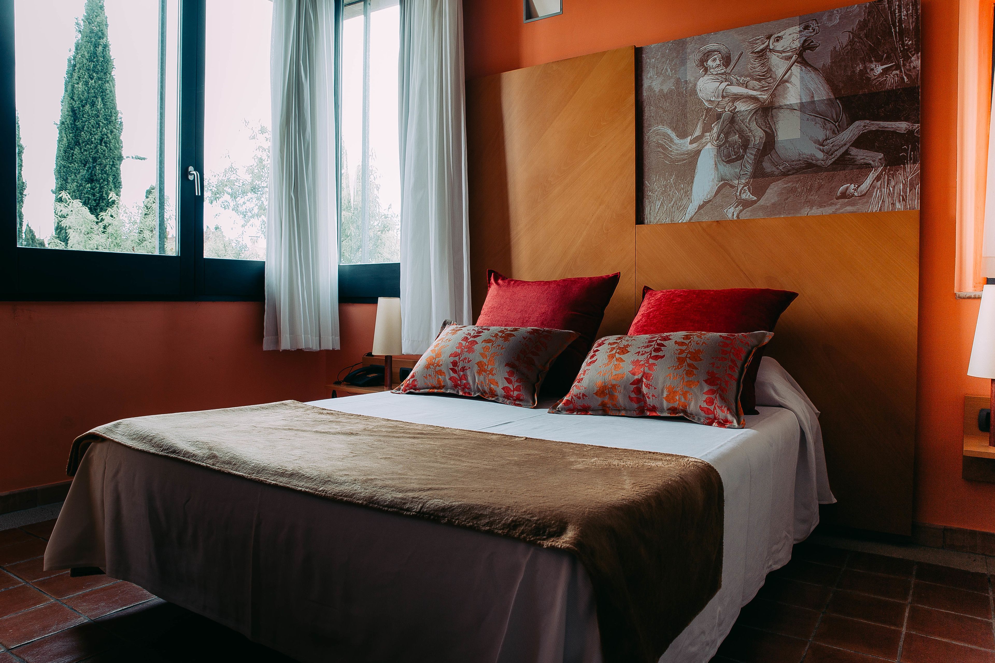 A bed with a brown bedspread, two red pillows, and a floral pillow.