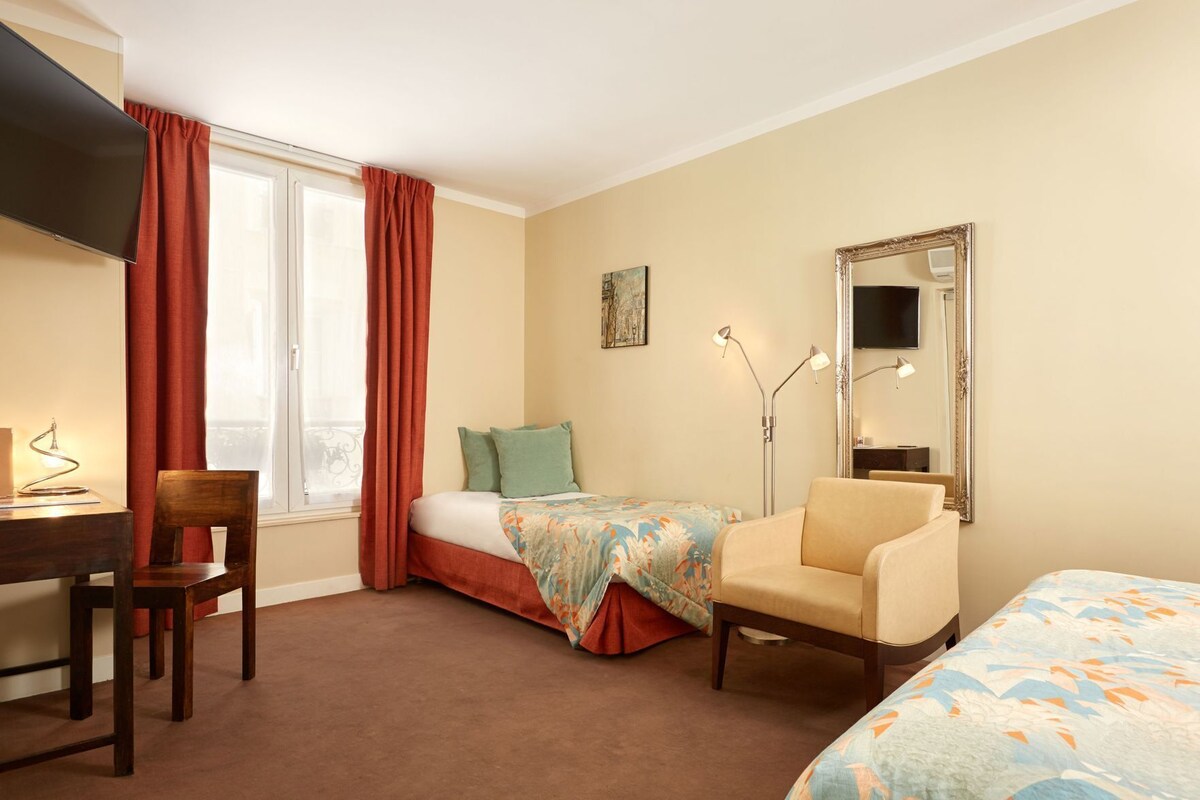 A hotel room with a bed, a desk, a chair, a TV, a mirror, and a window with curtains.