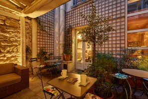 Une agréable terrasse extérieure avec un canapé en osier, une table avec des chaises et une plante en pot.
