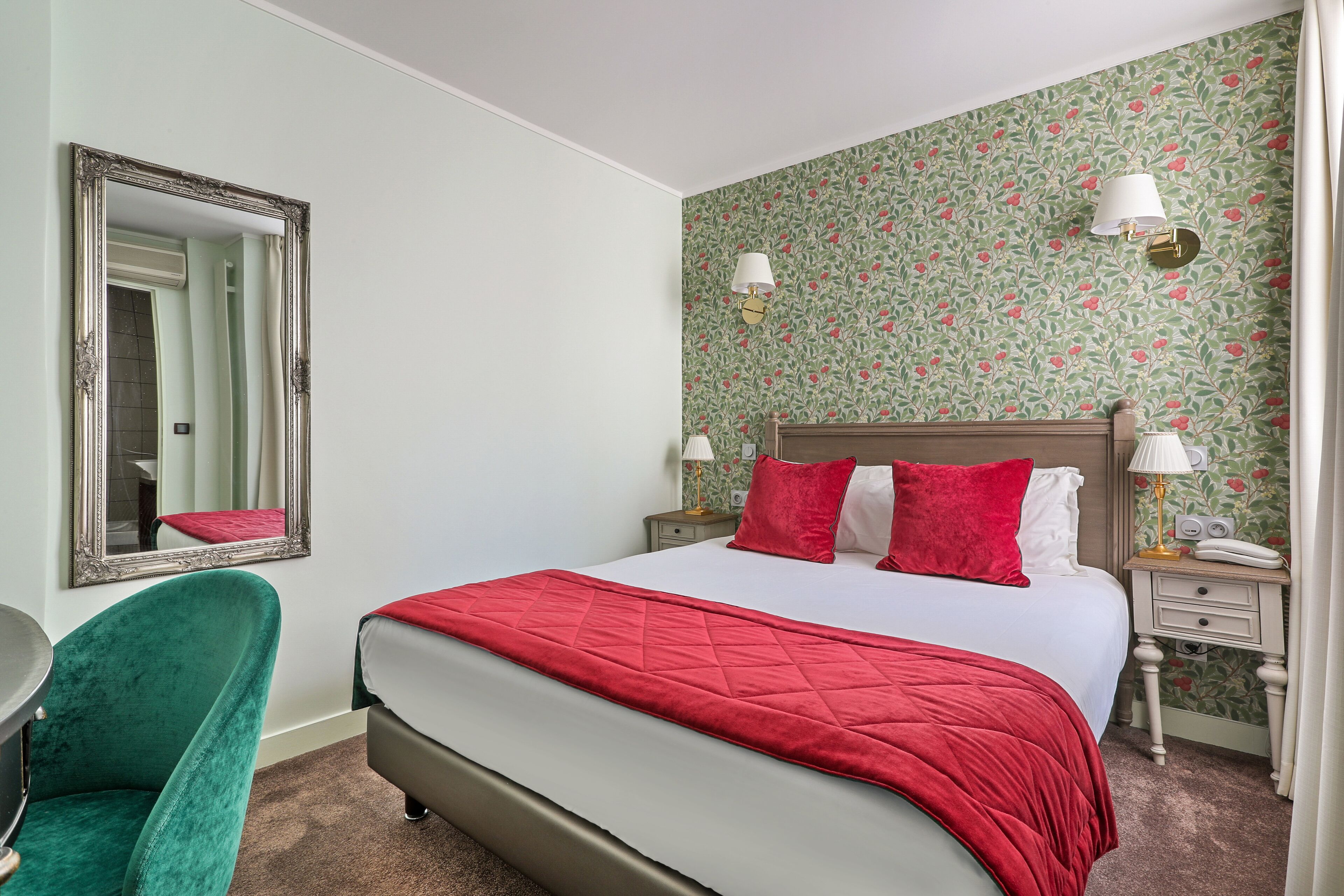A hotel room with a bed, a chair, a nightstand, a lamp, and a mirror.