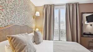 Et hotelværelse med en seng, puder, en lampe, et spejl og udsigt over byen gennem vinduet.