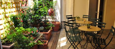 A patio with potted plants, a wooden table, and outdoor chairs.