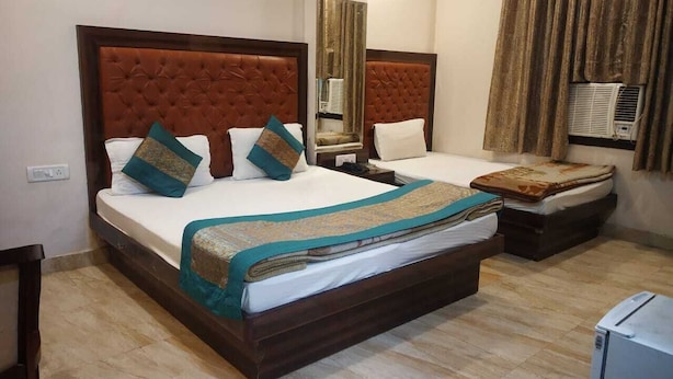 A hotel room with two beds, each with a tufted headboard, a large mirror, and an air conditioning unit. - Hotel Indo continental (New Delhi)