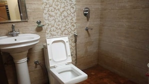 A bathroom with a pedestal sink, a toilet, and a shower. - Hotel Indo continental (New Delhi)
