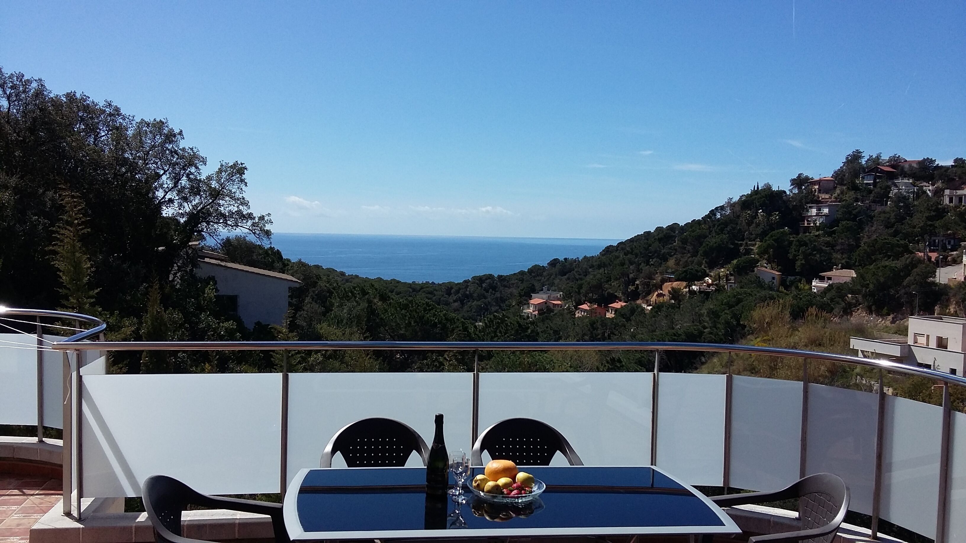 A balcony with a table set for two, overlooking a coastal view.