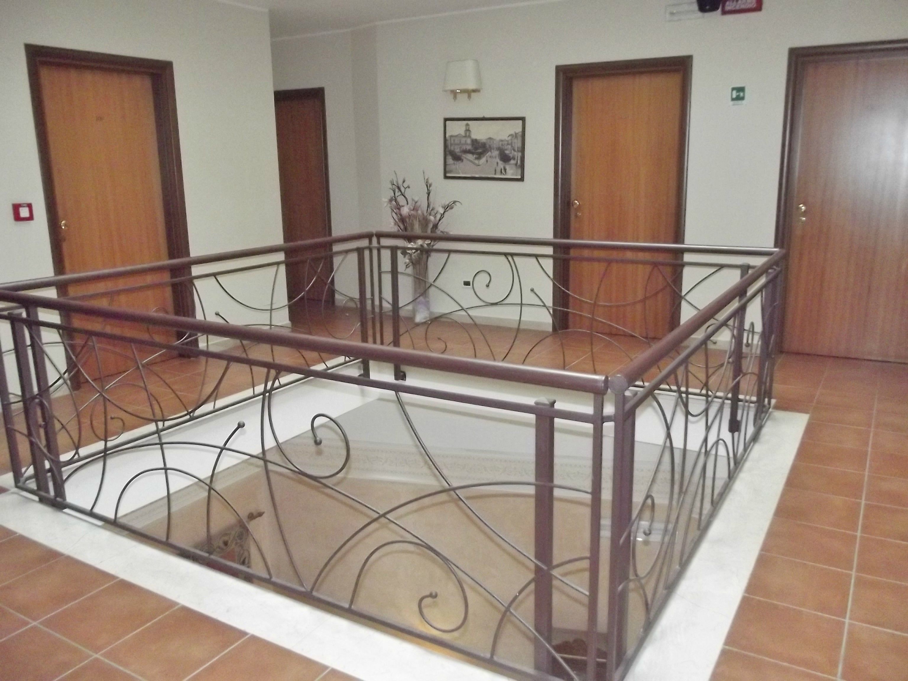 Un'ampia area interna con ringhiera in metallo, pavimento piastrellato e porte in legno.