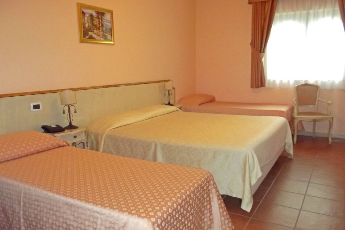 Une chambre d’hôtel avec deux lits simples, une table de chevet avec une lampe, une chaise et une fenêtre avec des rideaux.