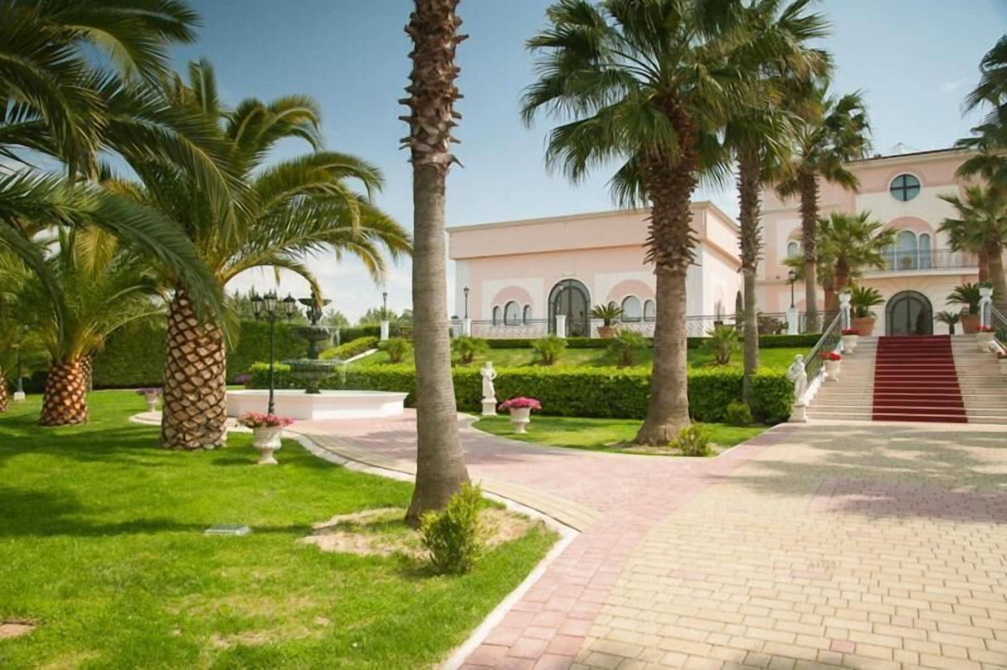 Un jardín cuidado con palmeras, un camino empedrado y un edificio con ventanas arqueadas.