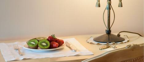 A dining table with a plate of sliced kiwi and strawberries, a fork, a knife, and a lamp.