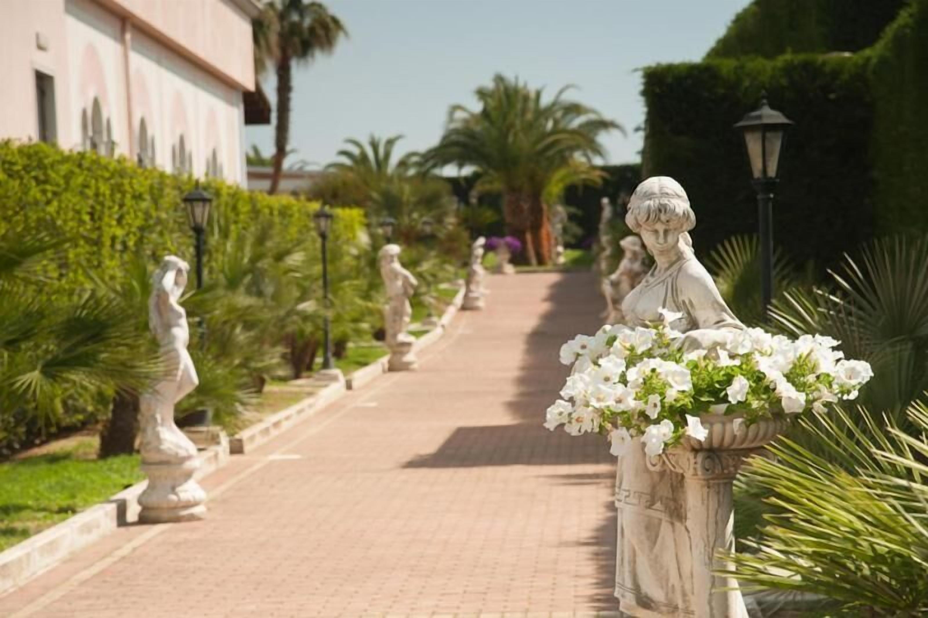 A pathway lined with statues and a fountain with white flowers.