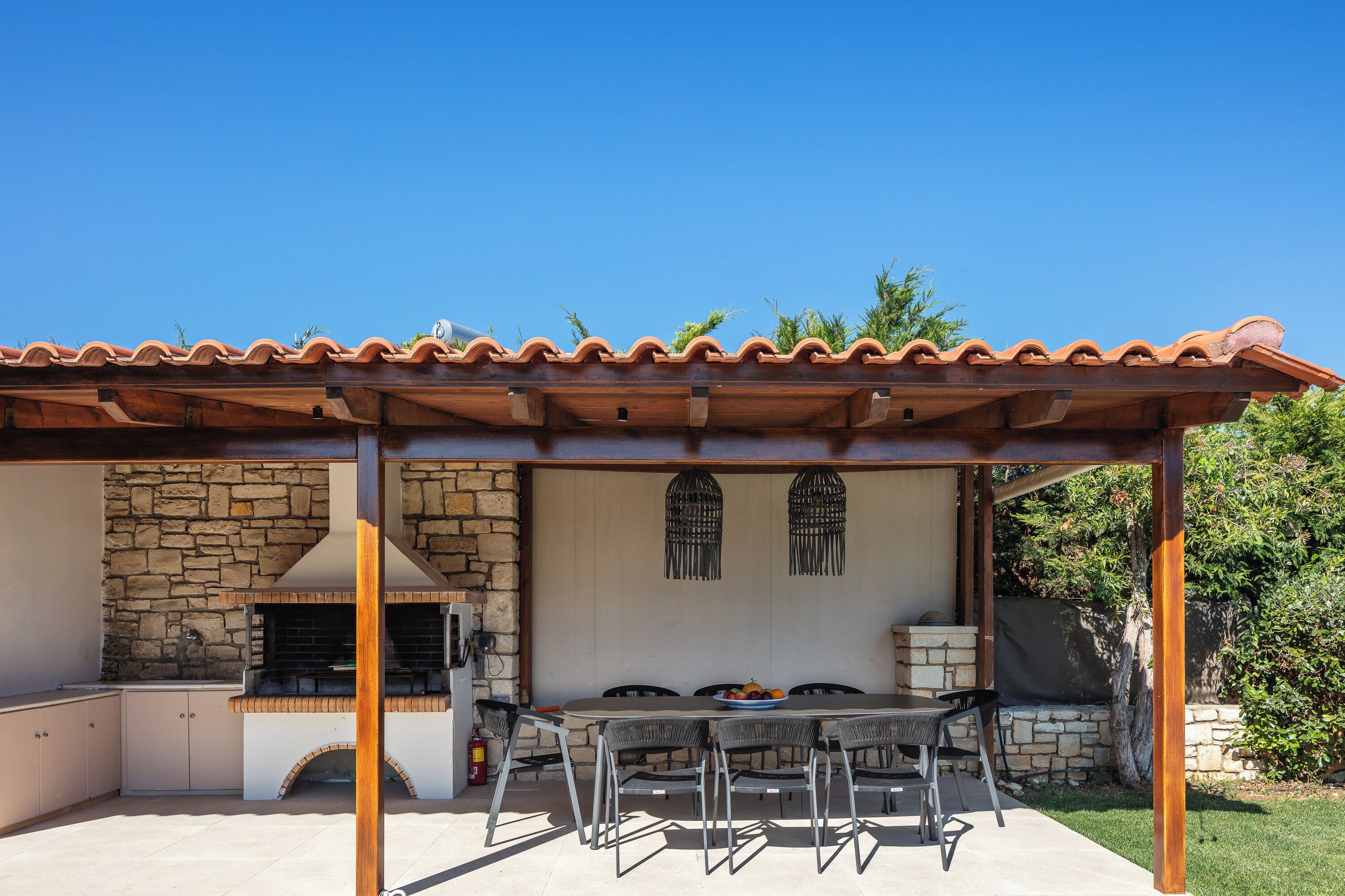 An outdoor patio with a stone wall, a grill, and a table with chairs.