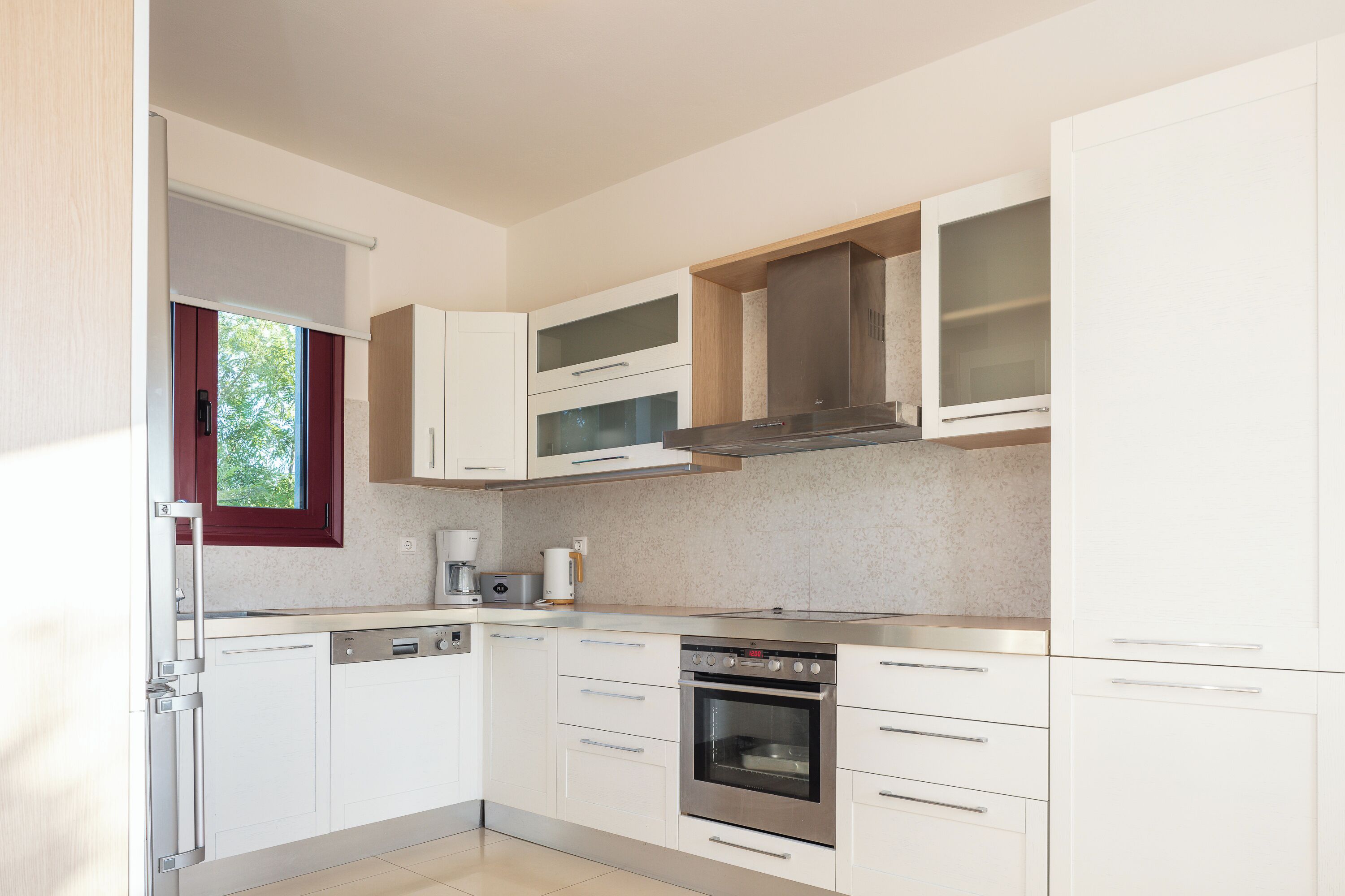 Cucina moderna con mobili bianchi, elettrodomestici in acciaio inossidabile e una finestra con tende rosse.