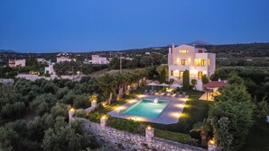 En modern villa med en swimmingpool, omgiven av frodig grönska och en stenmur.