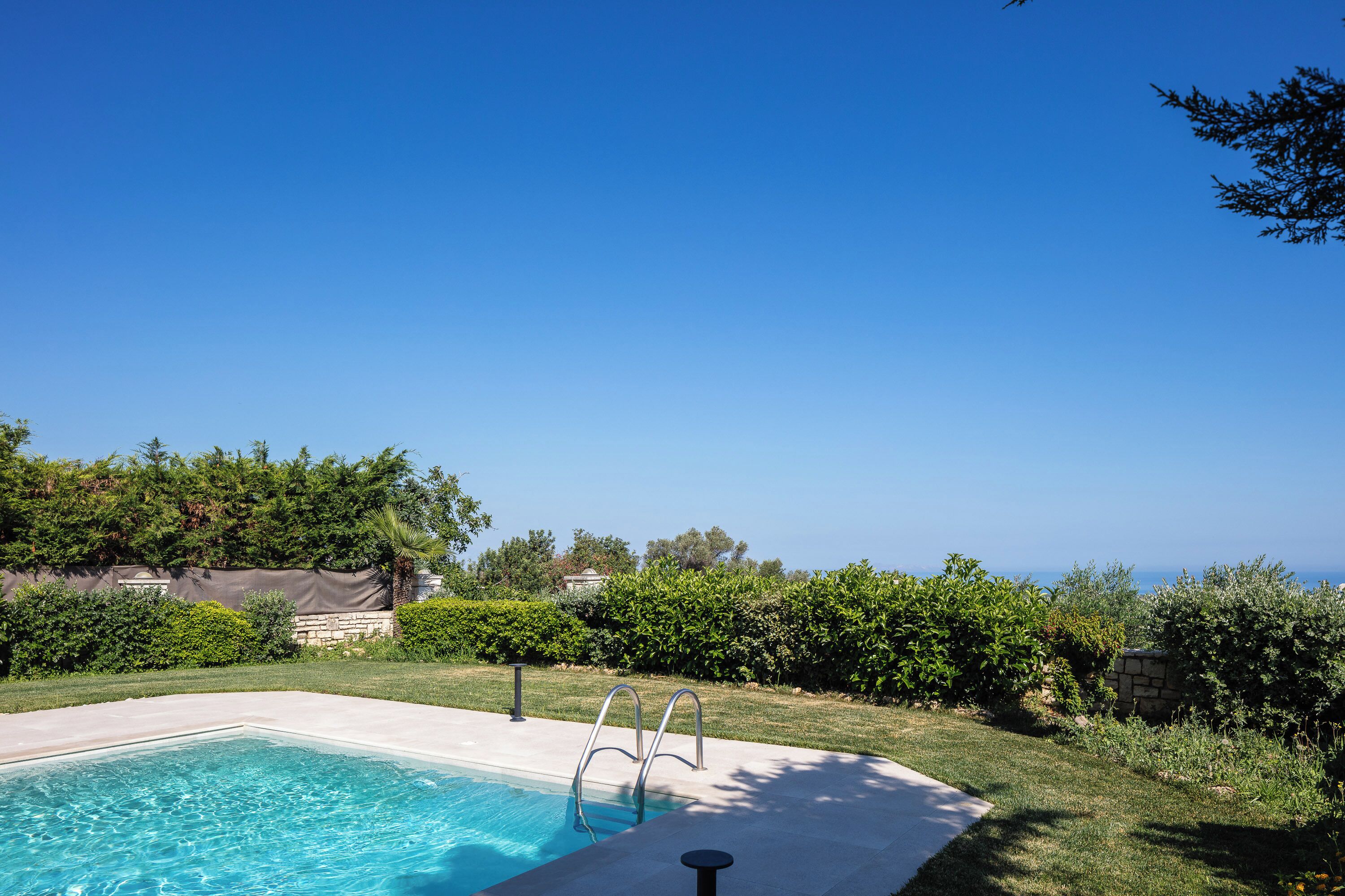 A rectangular swimming pool with a metal ladder, surrounded by a concrete deck.