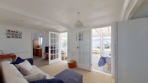 En rummelig stue med sofa, spisebord og udsigt til det fri gennem glasdøre.