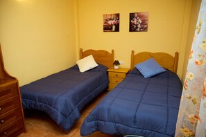 Ein Zimmer mit zwei Einzelbetten, Holz-Kopfteilen, einem Nachttisch mit Lampe und einem Holzkasten.
