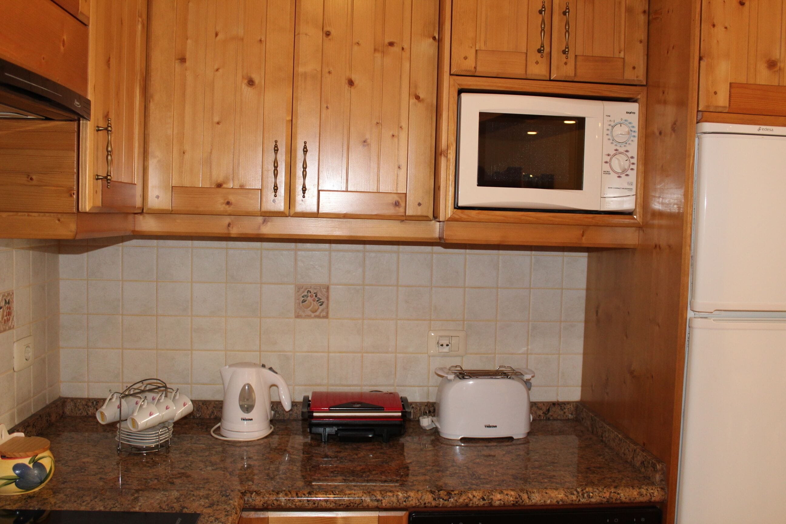 A kitchen with wooden cabinets, a microwave, a toaster, and a kettle on the countertop.