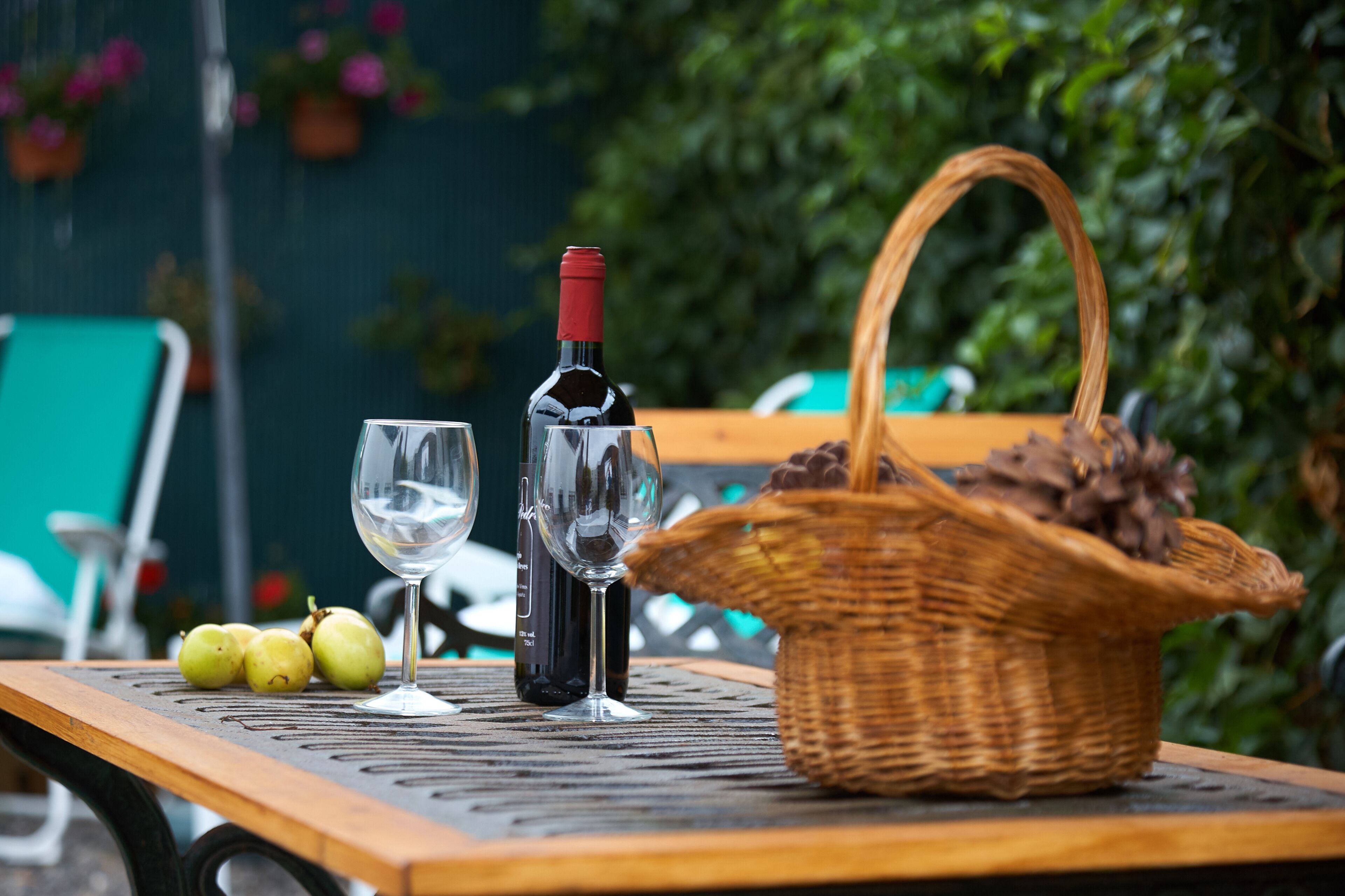 A table with a bottle of wine, two wine glasses, and a basket of pinecones.
