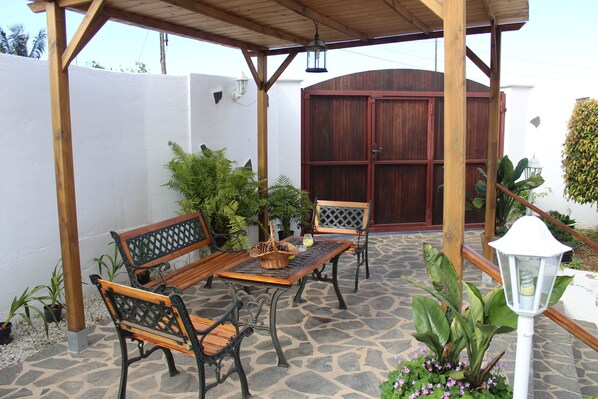 Eine Terrasse im Freien mit einem Holztisch und Bänken, umgeben von Blumentöpfen und einem Steinfußboden.