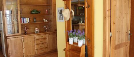 Una cocina de madera con armarios abiertos, un estante empotrado con plantas en macetas y una puerta con un abrigo colgado del pomo.
