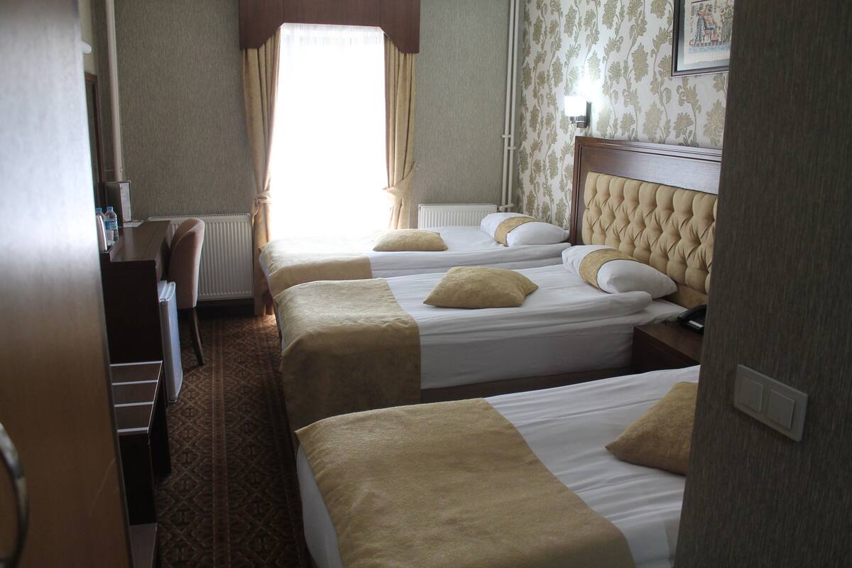 A hotel room with three beds, a desk, and a radiator.