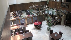 A spacious dining area with multiple tables and chairs, a central chandelier, and a staircase leading to an upper level. - Rest Hotel (Ankara)