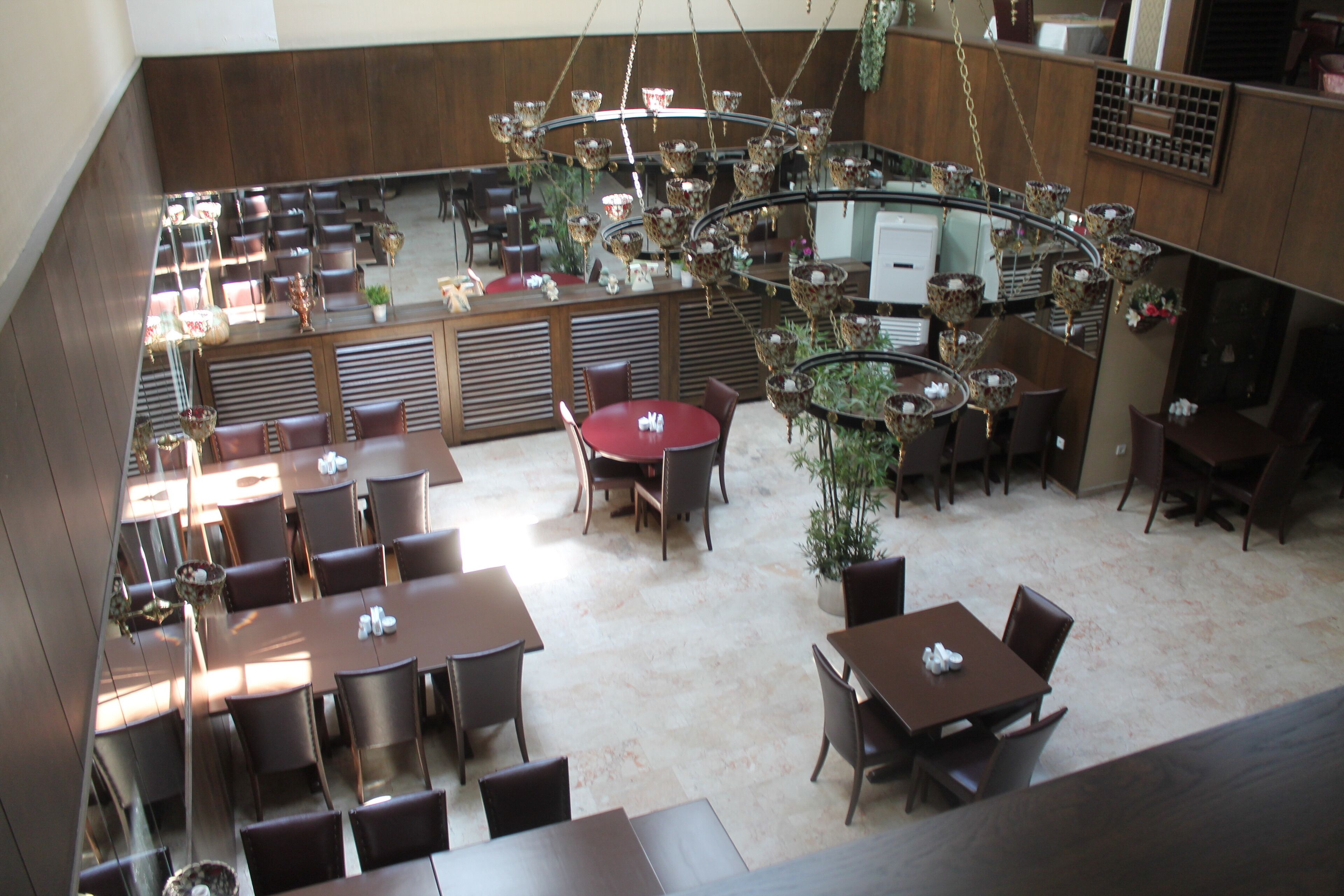 A spacious restaurant with multiple dining areas, including round and rectangular tables, and a central chandelier.