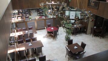 A spacious restaurant with multiple dining areas, including round and rectangular tables, and a central chandelier.