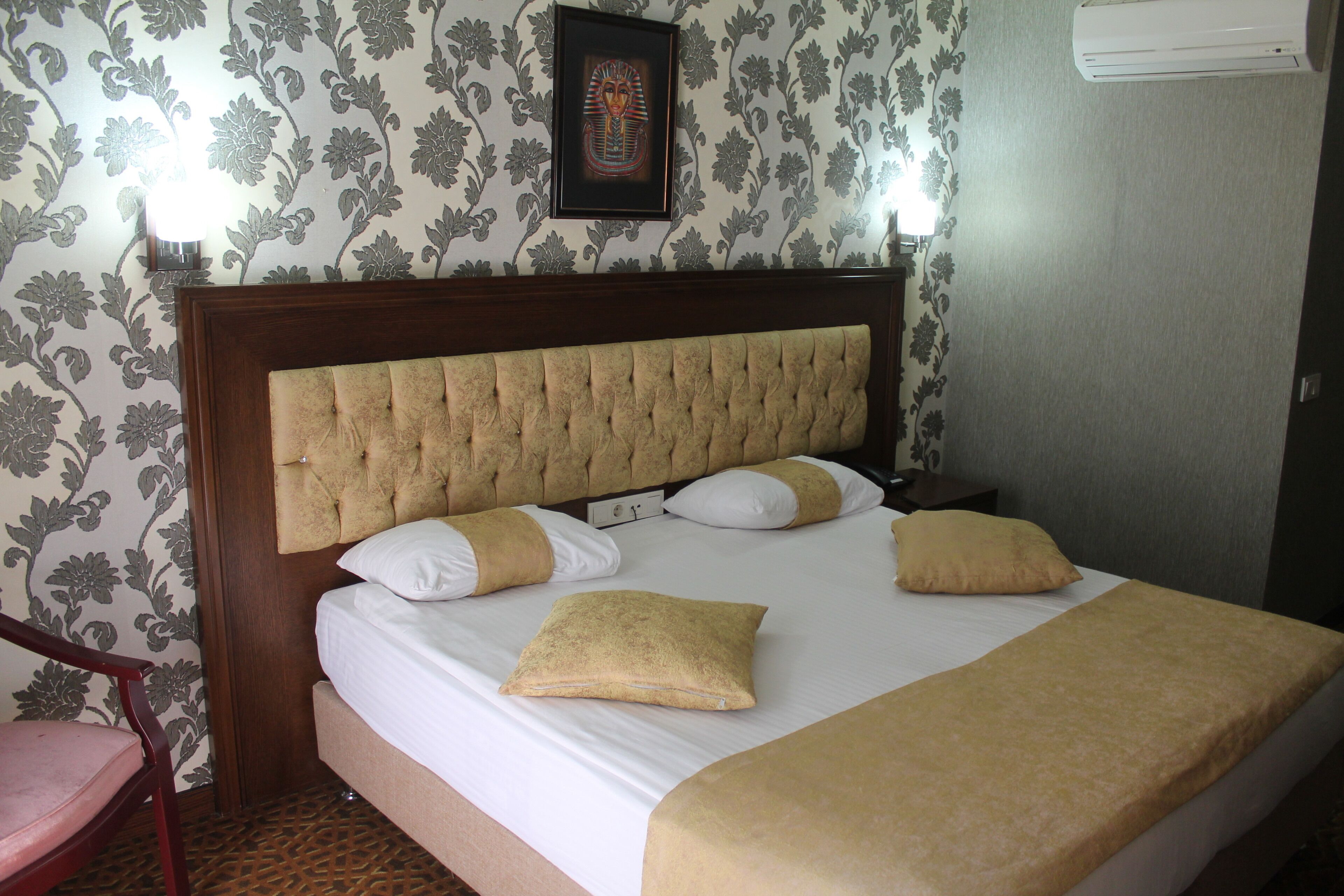 Una habitación de hotel con una cama grande, cabecera de madera, papel tapiz floral y un cuadro en la pared.