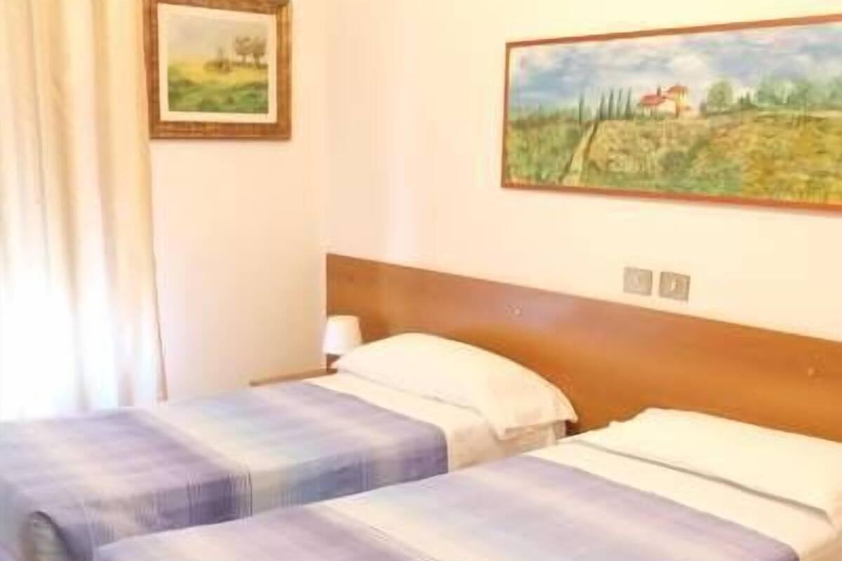 A room with two beds, a headboard, a painting, and a window with curtains.